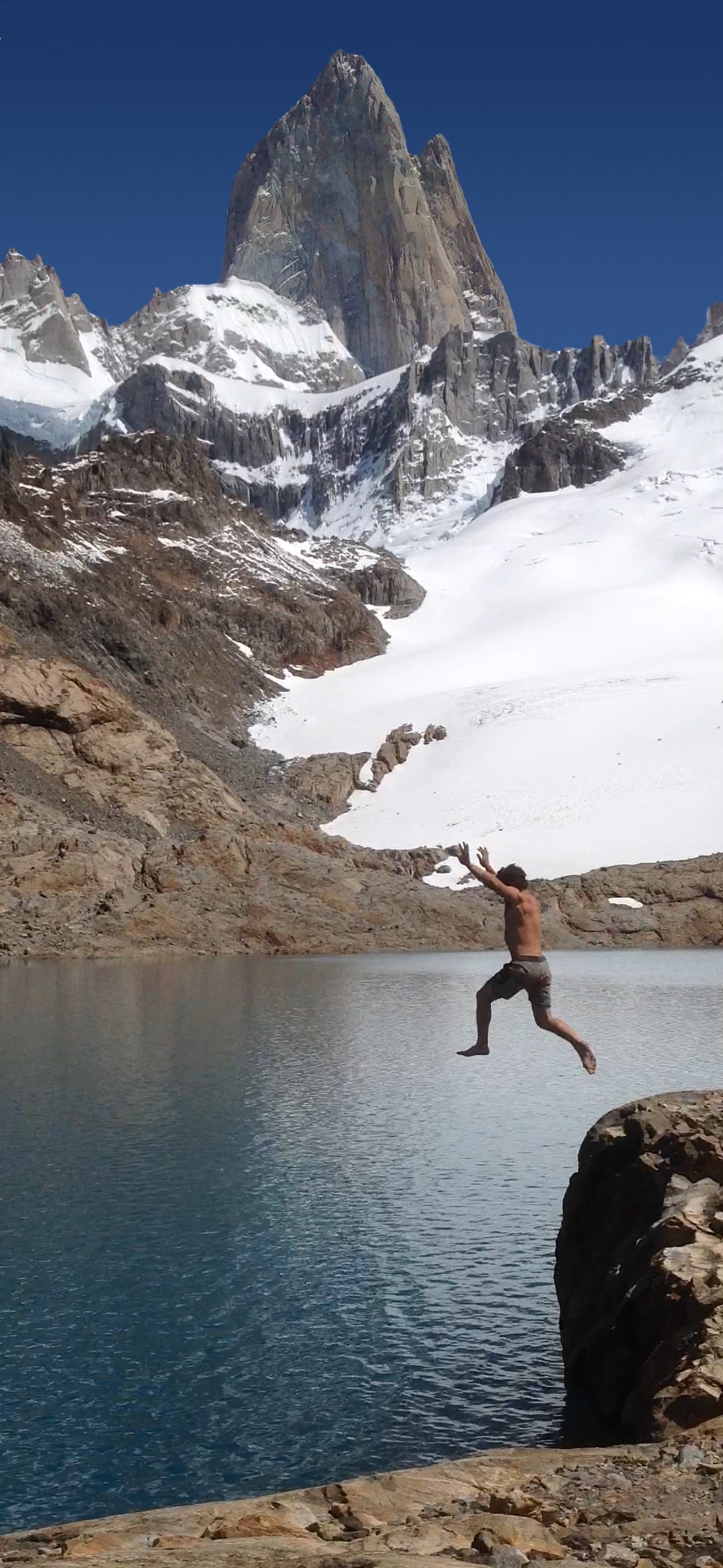 Leaping into a glacial lake below snowy granite peaks
