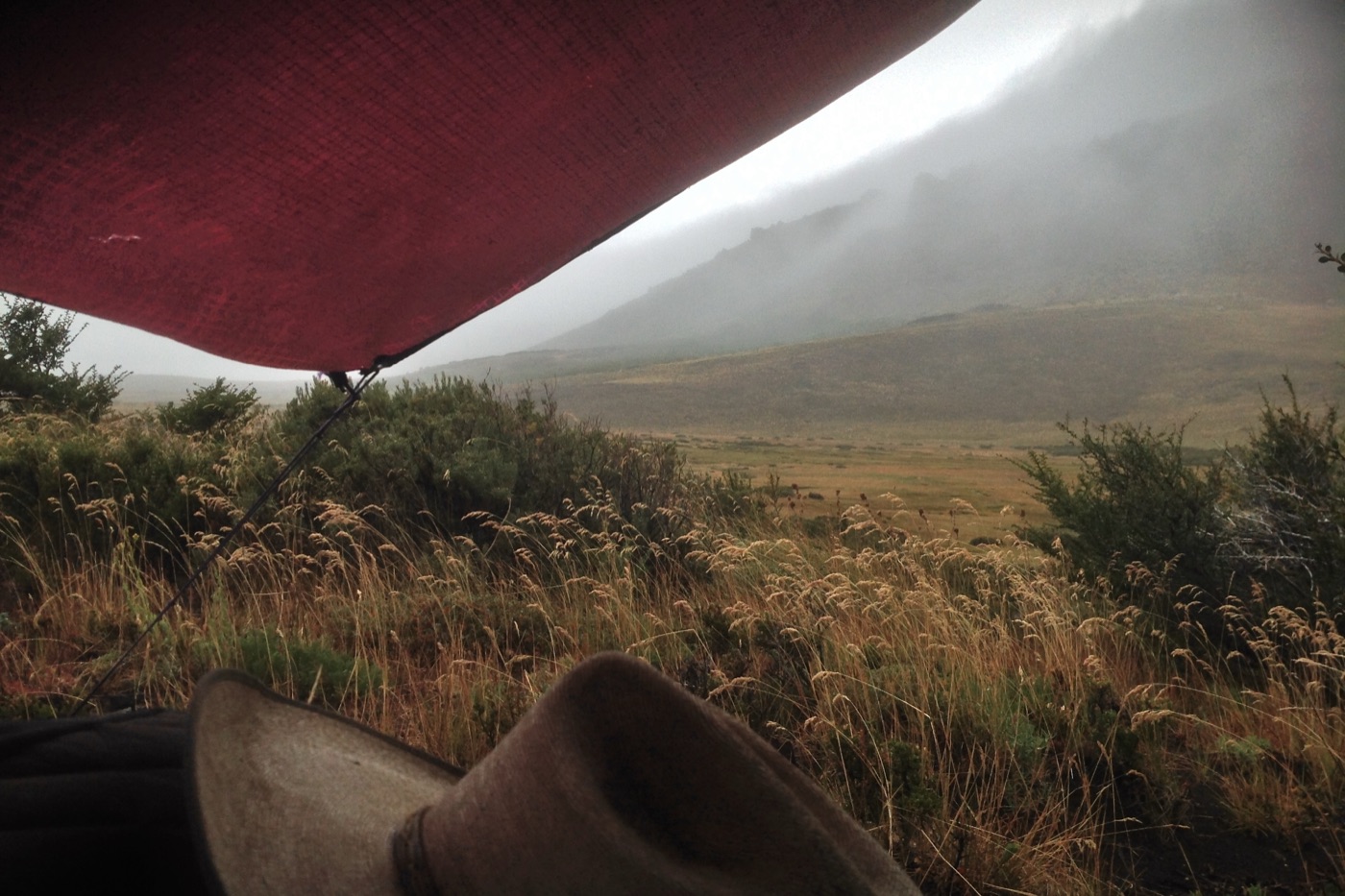A red tarp strung up as a shelter over a cowboy hat and sleeping bag in Patagonia